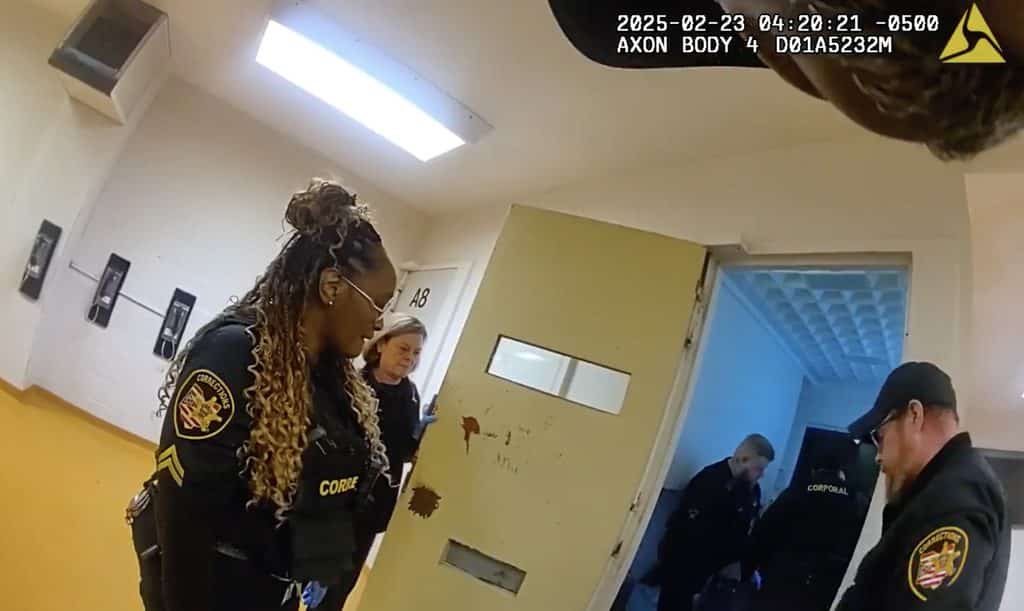 A still image from a body camera shows Jennifer Wade’s cell with three corrections officers standing outside and two standing inside. Her body is not visible.